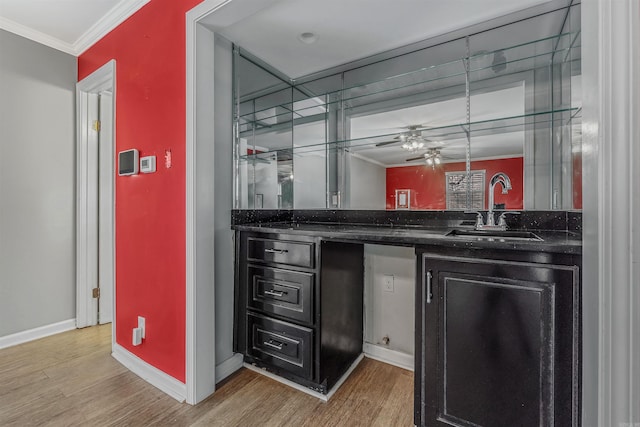 bar featuring light wood-style floors, baseboards, ornamental molding, and a sink