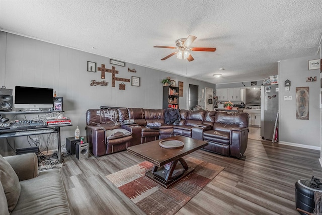 living area featuring ceiling fan, a textured ceiling, baseboards, and wood finished floors