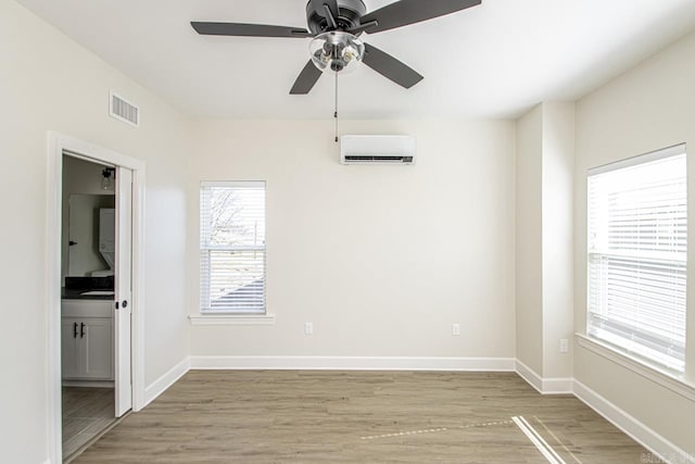 empty room featuring baseboards, a wall mounted air conditioner, visible vents, and light wood-style floors