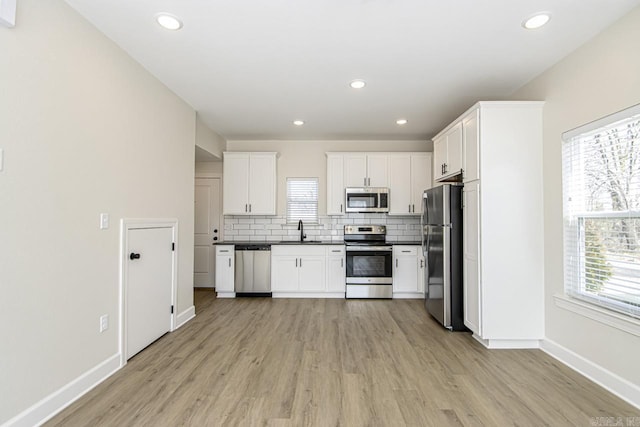 kitchen featuring dark countertops, a sink, stainless steel appliances, white cabinetry, and backsplash