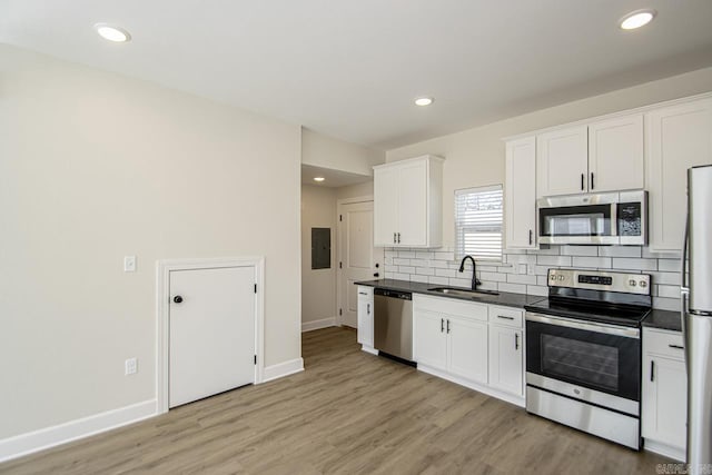 kitchen featuring dark countertops, a sink, stainless steel appliances, white cabinetry, and backsplash