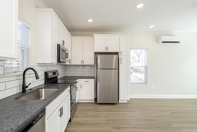 kitchen featuring decorative backsplash, appliances with stainless steel finishes, an AC wall unit, white cabinetry, and a sink