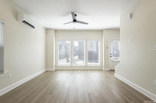 unfurnished living room featuring ceiling fan, baseboards, an AC wall unit, and wood finished floors