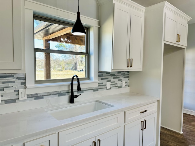 kitchen featuring light stone counters, decorative light fixtures, decorative backsplash, white cabinets, and a sink