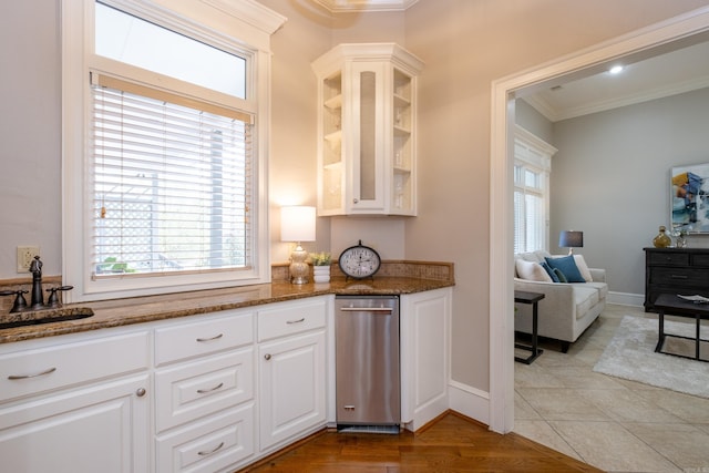 kitchen featuring ornamental molding, dark stone countertops, glass insert cabinets, and a healthy amount of sunlight