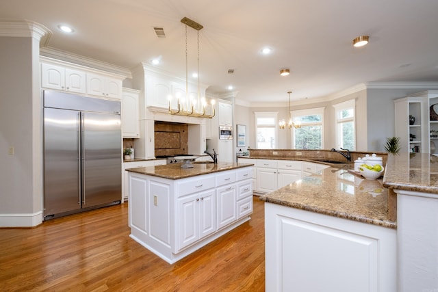 kitchen with built in appliances, a spacious island, a sink, and crown molding