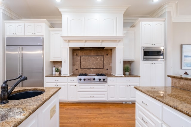 kitchen featuring light stone counters, light wood finished floors, ornamental molding, a sink, and built in appliances