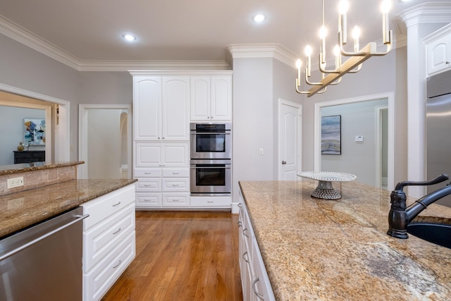 kitchen with light stone counters, stainless steel appliances, light wood-style flooring, ornamental molding, and a sink