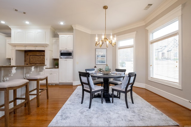 dining space with a chandelier, visible vents, crown molding, and wood finished floors