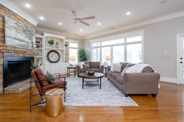 living area featuring baseboards, a stone fireplace, wood finished floors, and crown molding