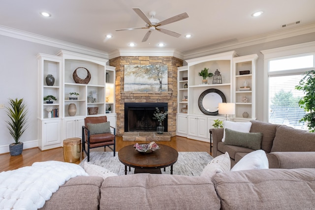 living room with ornamental molding, light wood-type flooring, visible vents, and a stone fireplace