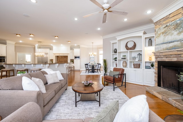 living room with light wood-type flooring, a healthy amount of sunlight, crown molding, and a stone fireplace