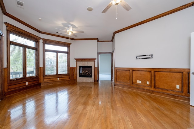 unfurnished living room featuring light wood-style flooring, a ceiling fan, visible vents, wainscoting, and crown molding