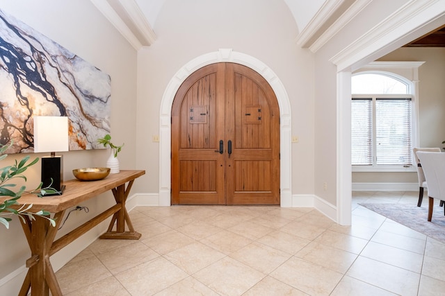 entryway featuring ornamental molding, arched walkways, vaulted ceiling, and light tile patterned floors