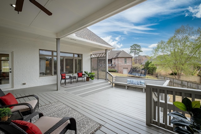 wooden deck featuring ceiling fan, a trampoline, and fence