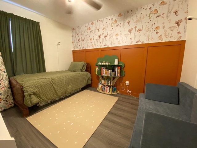 bedroom with a decorative wall, a wainscoted wall, wood finished floors, a ceiling fan, and wallpapered walls