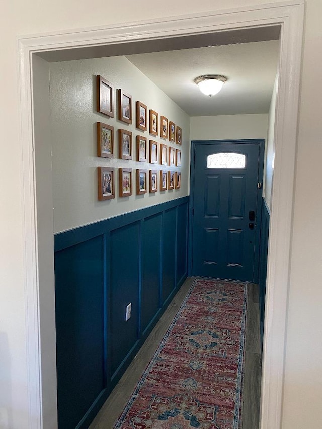 doorway featuring dark wood finished floors, a wainscoted wall, and a decorative wall