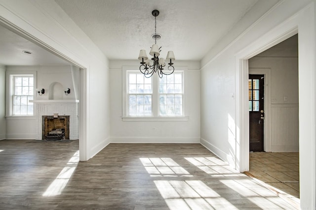 unfurnished dining area with a brick fireplace, a notable chandelier, a textured ceiling, and wood finished floors
