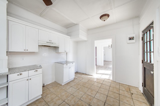 kitchen with decorative backsplash, wainscoting, white cabinets, light stone countertops, and under cabinet range hood