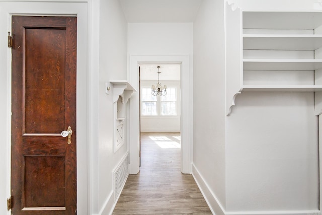 hall with baseboards, visible vents, a chandelier, and wood finished floors