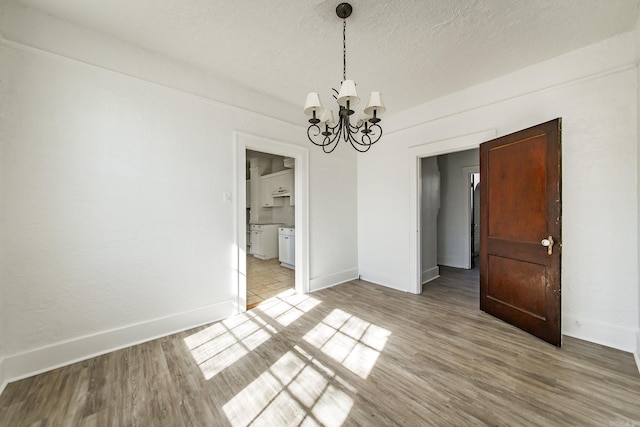 unfurnished dining area featuring light wood-style floors, baseboards, a chandelier, and a textured ceiling