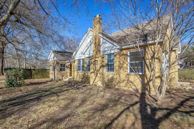 view of front facade featuring brick siding, fence, and a chimney