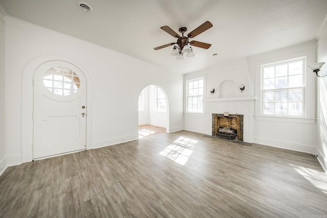 unfurnished living room with a brick fireplace, visible vents, arched walkways, and wood finished floors