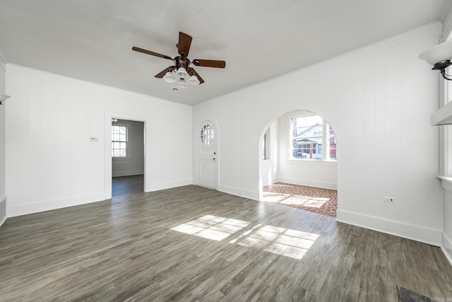 unfurnished living room with arched walkways, wood finished floors, a wealth of natural light, and a ceiling fan