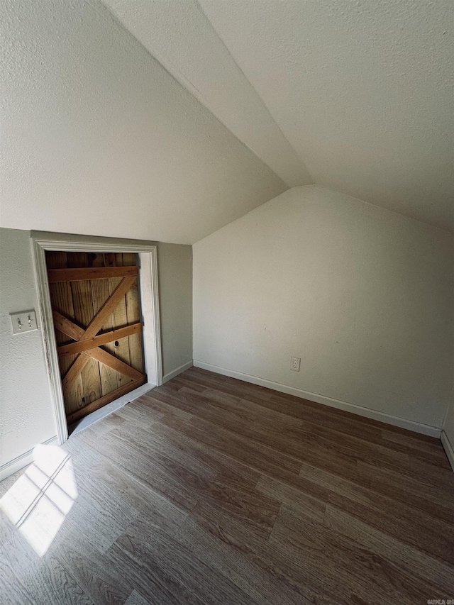 interior space with vaulted ceiling, a textured ceiling, wood finished floors, and baseboards