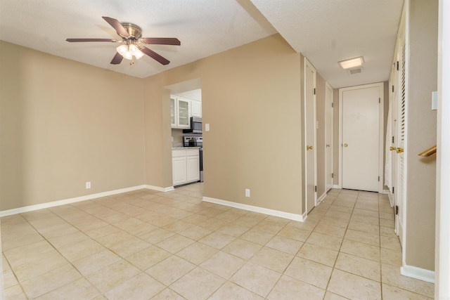 empty room featuring a textured ceiling, light tile patterned floors, a ceiling fan, and baseboards