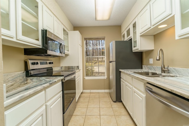 kitchen with light tile patterned floors, appliances with stainless steel finishes, a sink, and glass insert cabinets