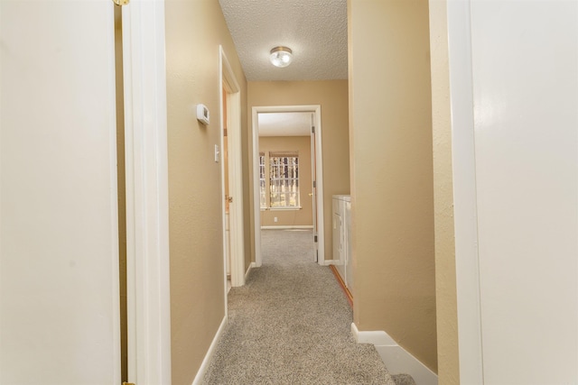 corridor with light carpet, a textured ceiling, and baseboards