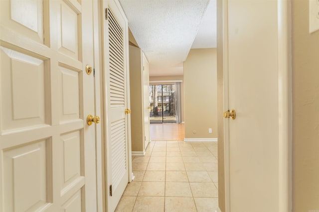 hall featuring a textured ceiling, baseboards, and light tile patterned floors