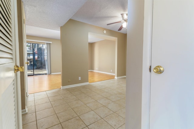 unfurnished room featuring light tile patterned floors, ceiling fan, a textured ceiling, and baseboards