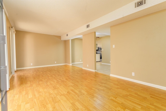 empty room with light wood-type flooring, visible vents, and baseboards