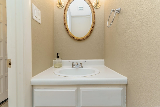 bathroom with vanity, visible vents, and a textured wall