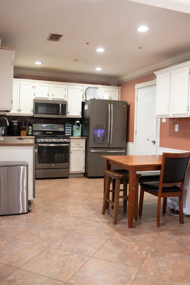 kitchen featuring a sink, white cabinets, appliances with stainless steel finishes, decorative backsplash, and crown molding