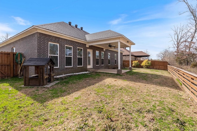 back of property featuring a fenced backyard, brick siding, a ceiling fan, a yard, and a patio area