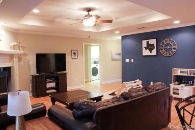 living room with baseboards, a fireplace, washer / clothes dryer, a raised ceiling, and a ceiling fan