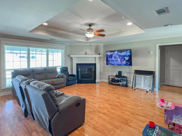 living area featuring visible vents, a raised ceiling, a fireplace with flush hearth, and wood finished floors