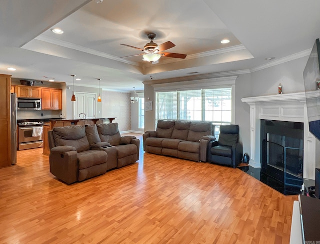 living room with light wood-type flooring, a raised ceiling, ornamental molding, and a tile fireplace