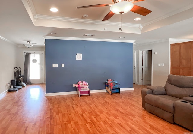 living room with baseboards, a raised ceiling, light wood-style flooring, and ornamental molding