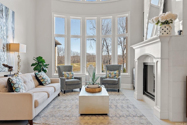 living area featuring a fireplace with flush hearth, light tile patterned flooring, and a towering ceiling