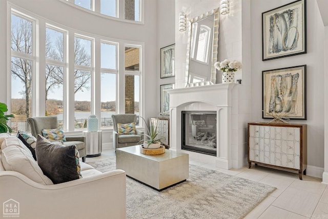 living room featuring a high ceiling, a water view, baseboards, tile patterned floors, and a glass covered fireplace