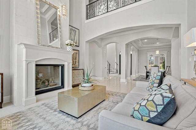 living area featuring baseboards, arched walkways, a glass covered fireplace, stairs, and crown molding