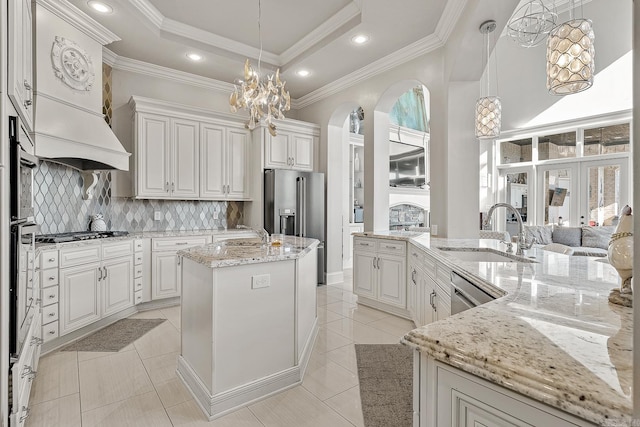 kitchen with a center island with sink, appliances with stainless steel finishes, a tray ceiling, crown molding, and a sink