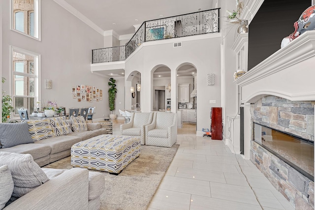 living room with arched walkways, a fireplace, visible vents, a high ceiling, and ornamental molding