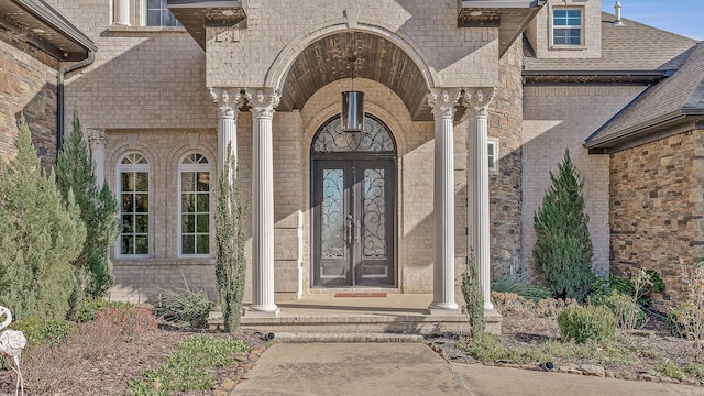 doorway to property featuring brick siding, roof with shingles, and french doors