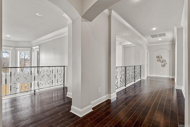 hall with baseboards, wood finished floors, visible vents, and crown molding