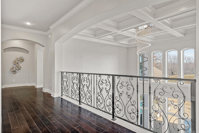 corridor featuring arched walkways, coffered ceiling, wood finished floors, beamed ceiling, and crown molding